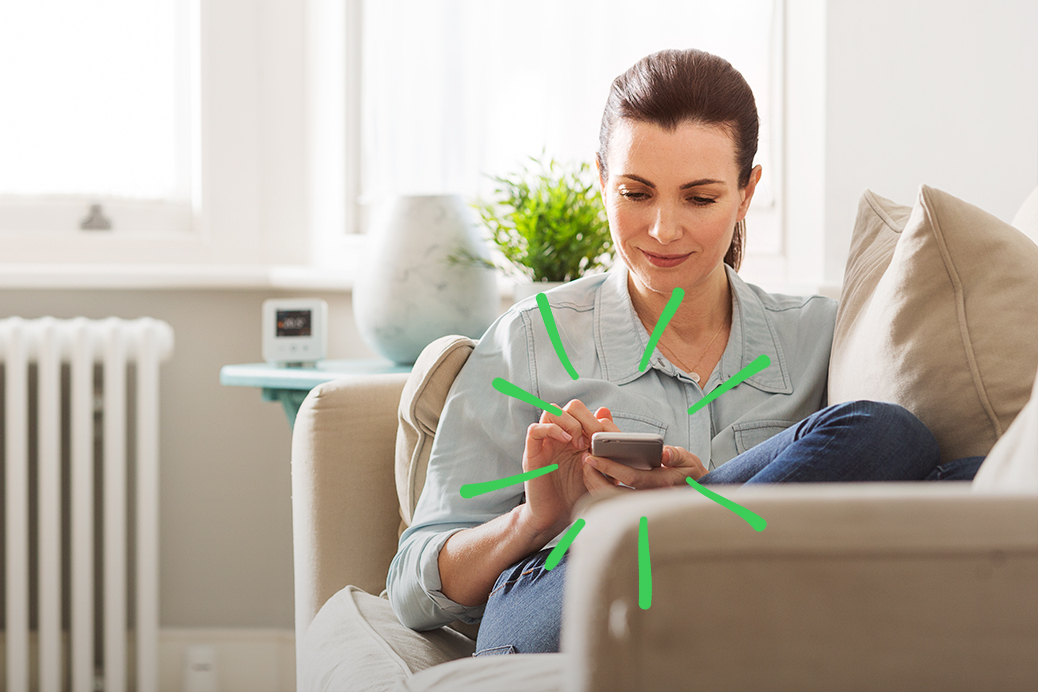 Woman sitting on the couch using the Wiser home heating app on her mobile phone